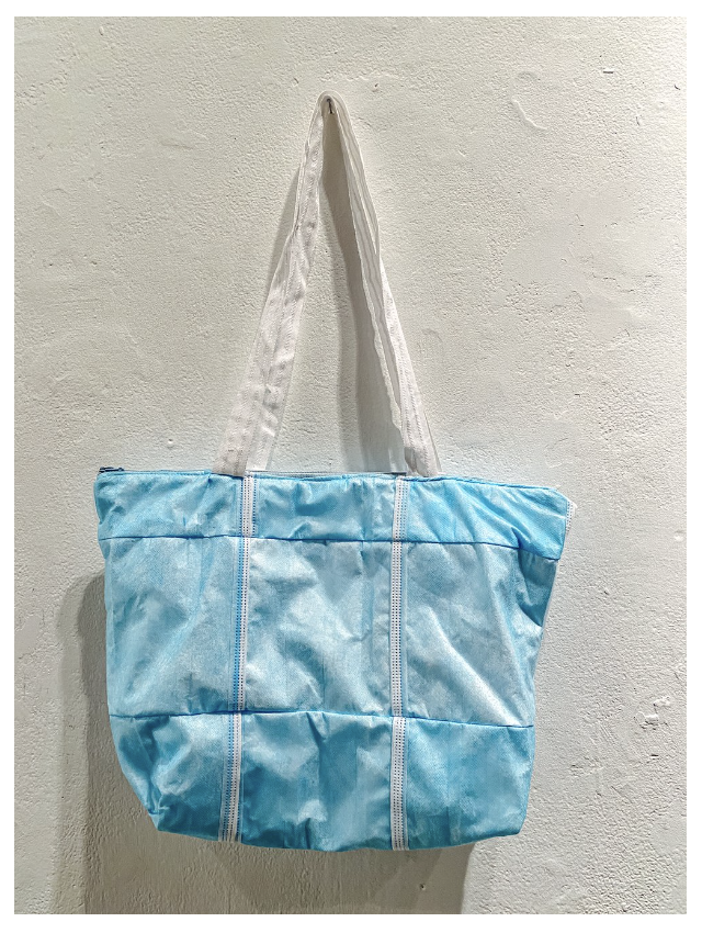 A blue tote bag made from medical masks hangs from a white wall.